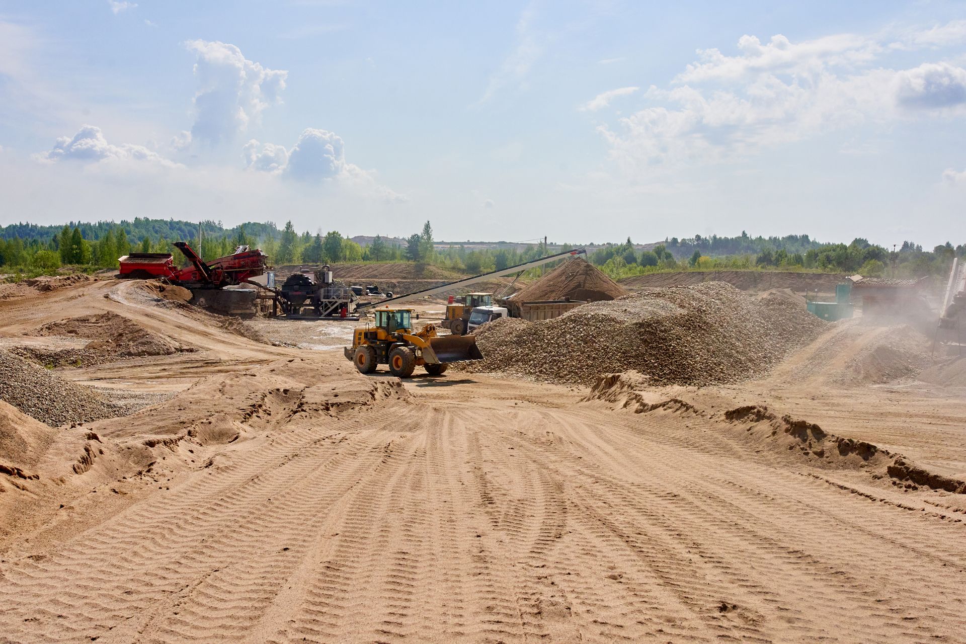 Construction site with heavy machinery moving sand under a bright sky.