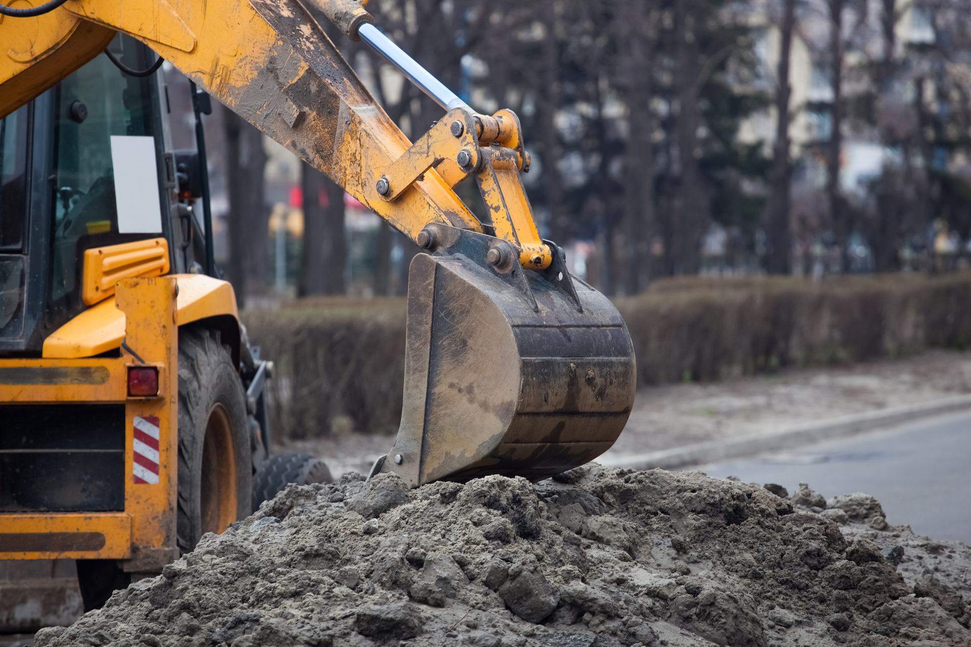Yellow backhoe bucket scooping up dirt on a road.