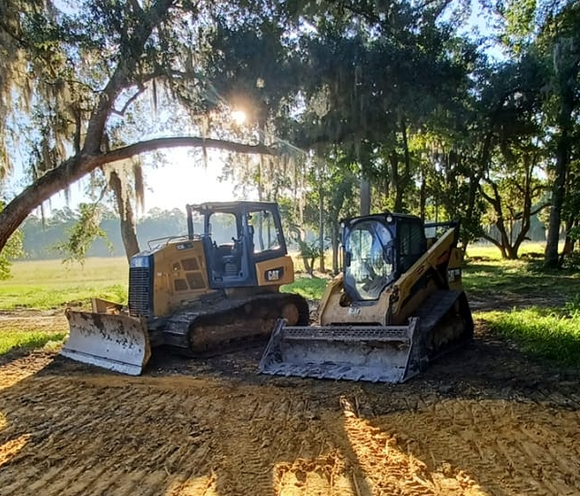 Two yellow Caterpillar construction machines in a clearing under trees, sunlight shining. Two yellow Caterpillar construction machines in a clearing under trees, sunlight shining.