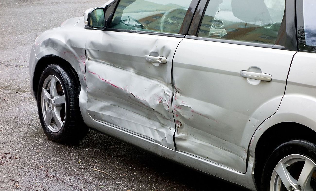 Silver sedan with a heavily dented side panel and damaged front fender on a wet road
