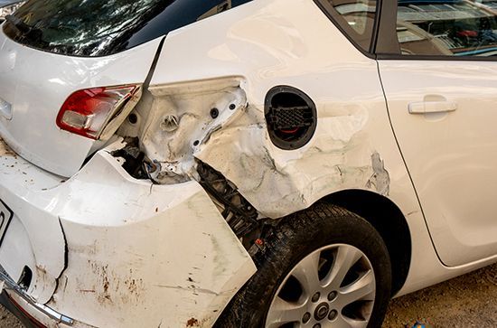 White car with severe rear-side collision damage and crumpled body panels