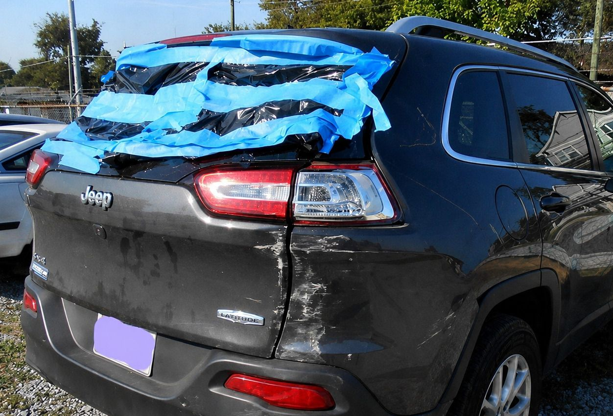 Black SUV with rear-window damage and blue plastic covering the broken glass.