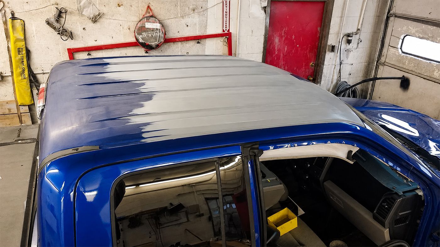 A blue Plymouth Prowler with its hood open in a garage. A red car is visible in the background.