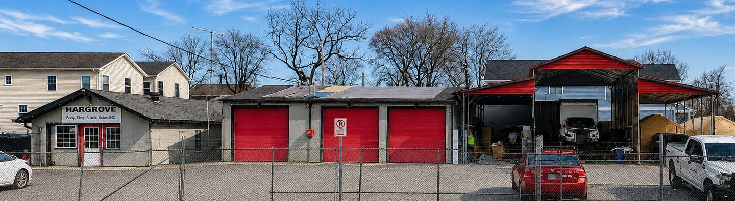 Hargrove autobody with garage bays and a parked red car on a cobblestone street under a blue sky.