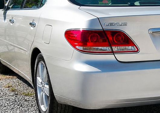 Silver sedan rear side view parked on gravel, with red taillight and chrome trim.