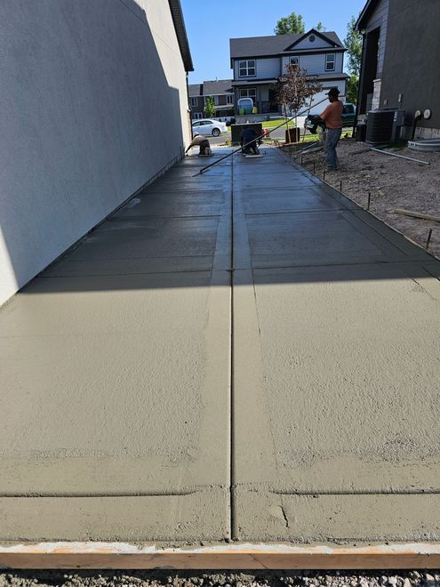 A freshly poured, textured concrete walkway between two houses, with a worker visible in the distance.