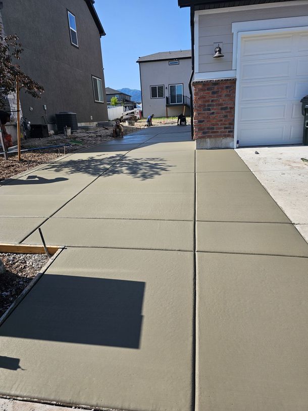 A newly poured concrete driveway leads between two houses on a bright, sunny day.