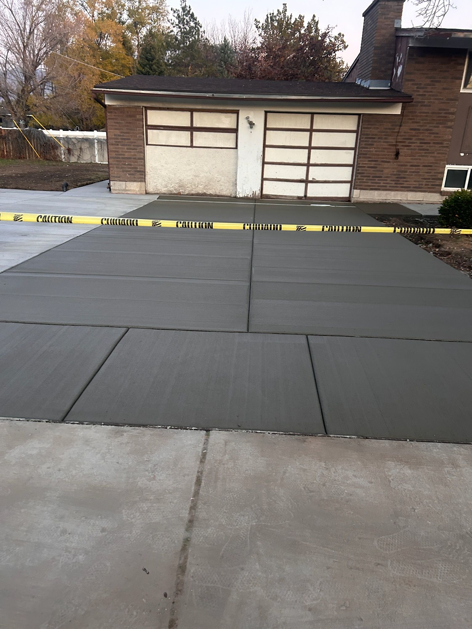 Interlocking dark gray floor mats laid out on a concrete driveway in front of a garage, blocked off by yellow caution tape.