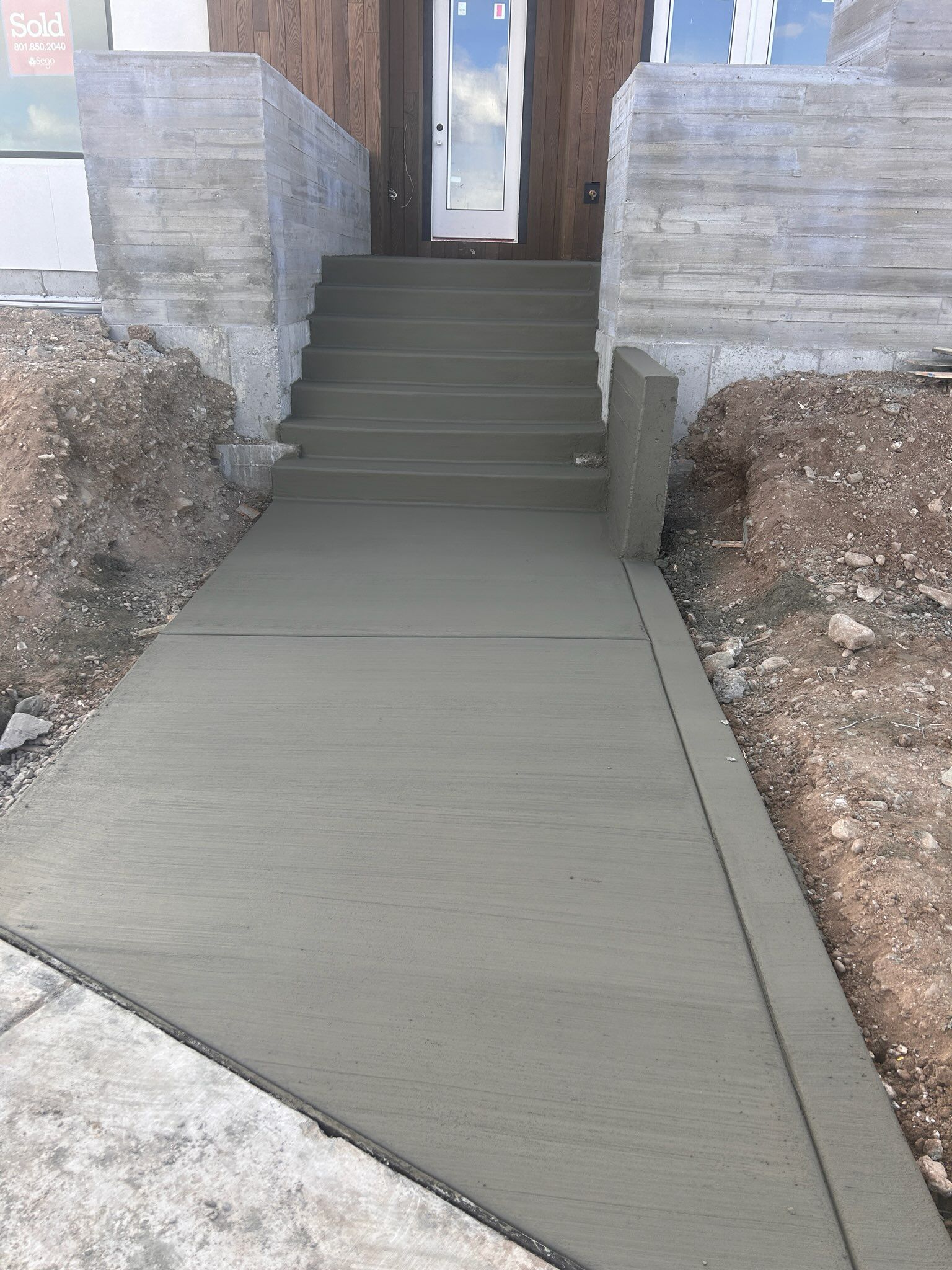 A concrete walkway leads up a flight of stairs to an entryway with a light-colored door and stone-textured walls.
