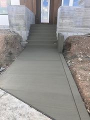 A concrete walkway leads up a flight of stairs to an entryway with a light-colored door and stone-textured walls.