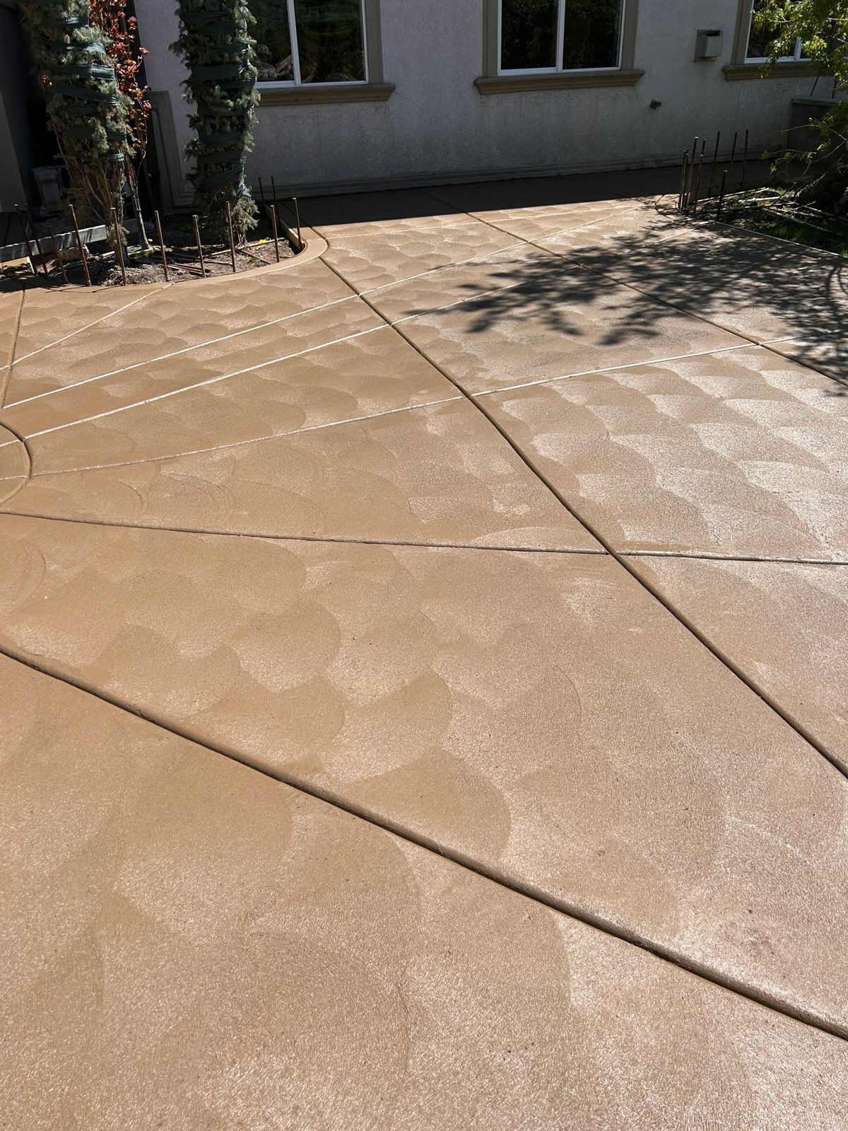 Tan concrete driveway with overlapping circular patterns caused by cleaning or pressure washing.