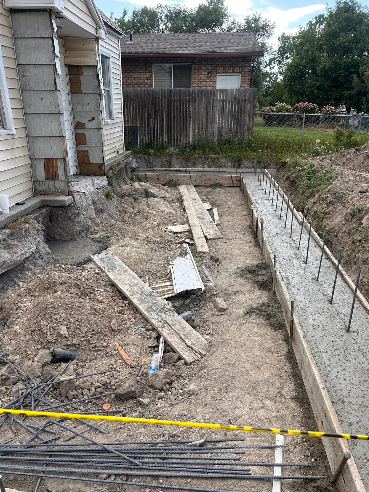 Concrete foundation forms and steel rebar stakes installed in a trench alongside a house under construction.
