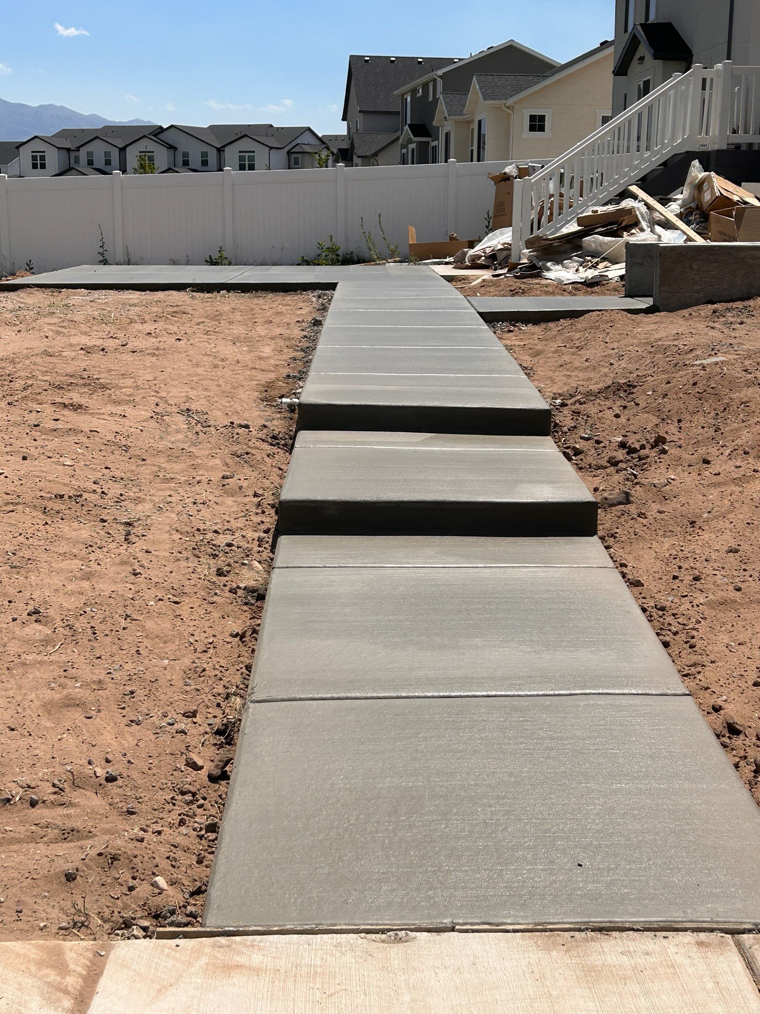 A concrete walkway with multiple steps leading up toward a house under construction in a residential neighborhood.