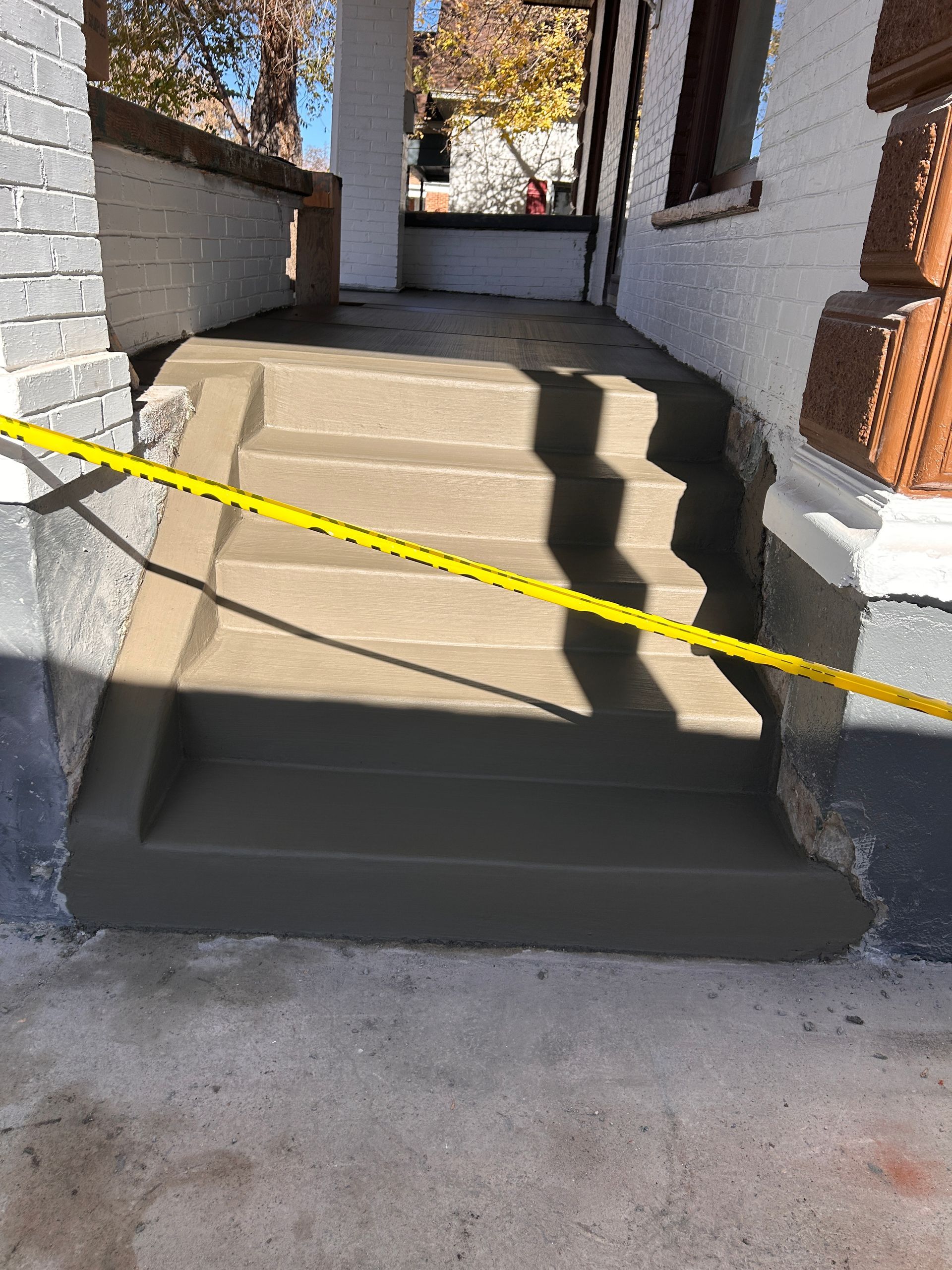 Freshly poured concrete steps at the entrance of a house, blocked off by yellow caution tape.