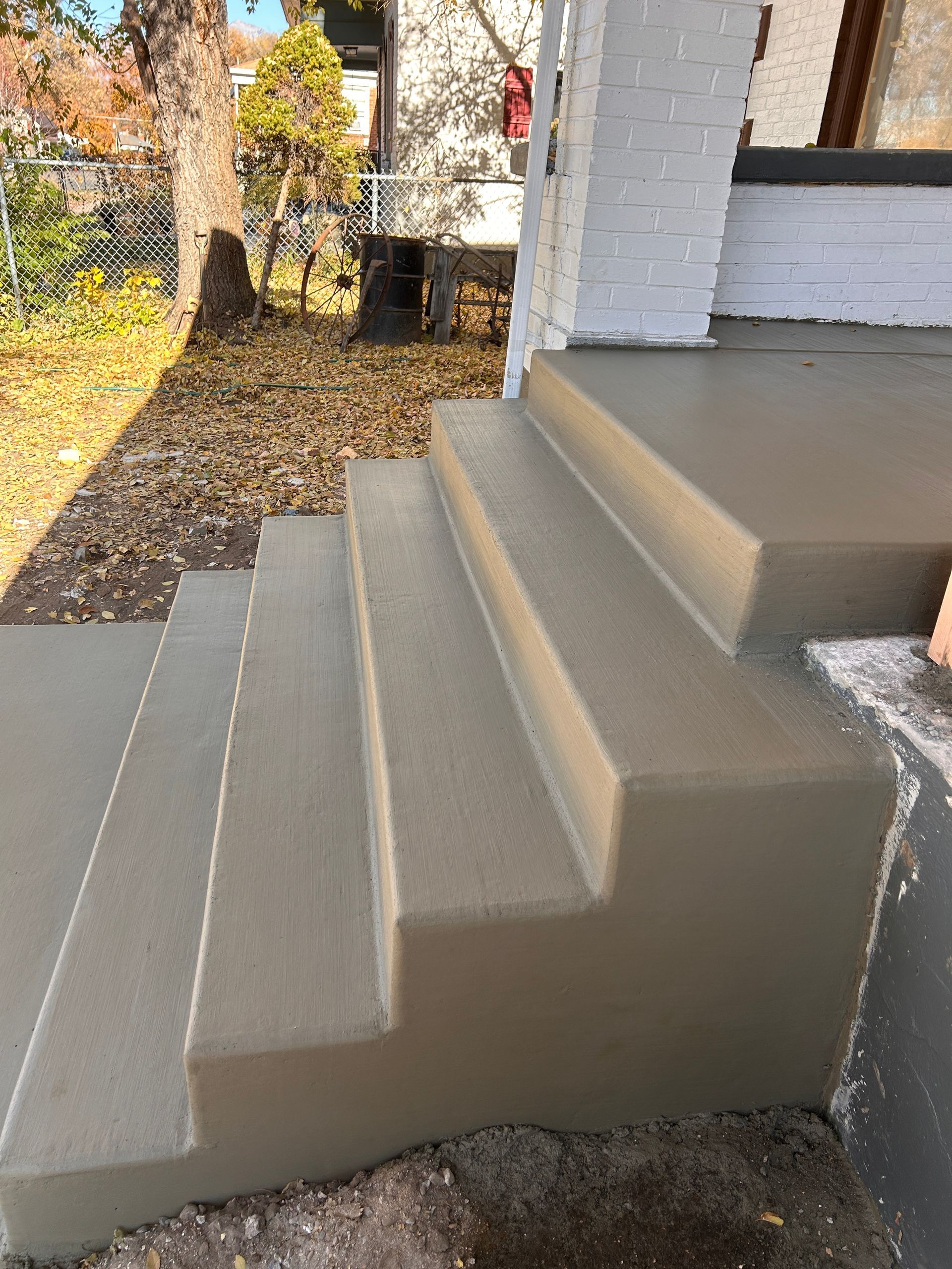 A set of newly poured, smooth gray concrete steps leading up to a porch in an outdoor residential setting.