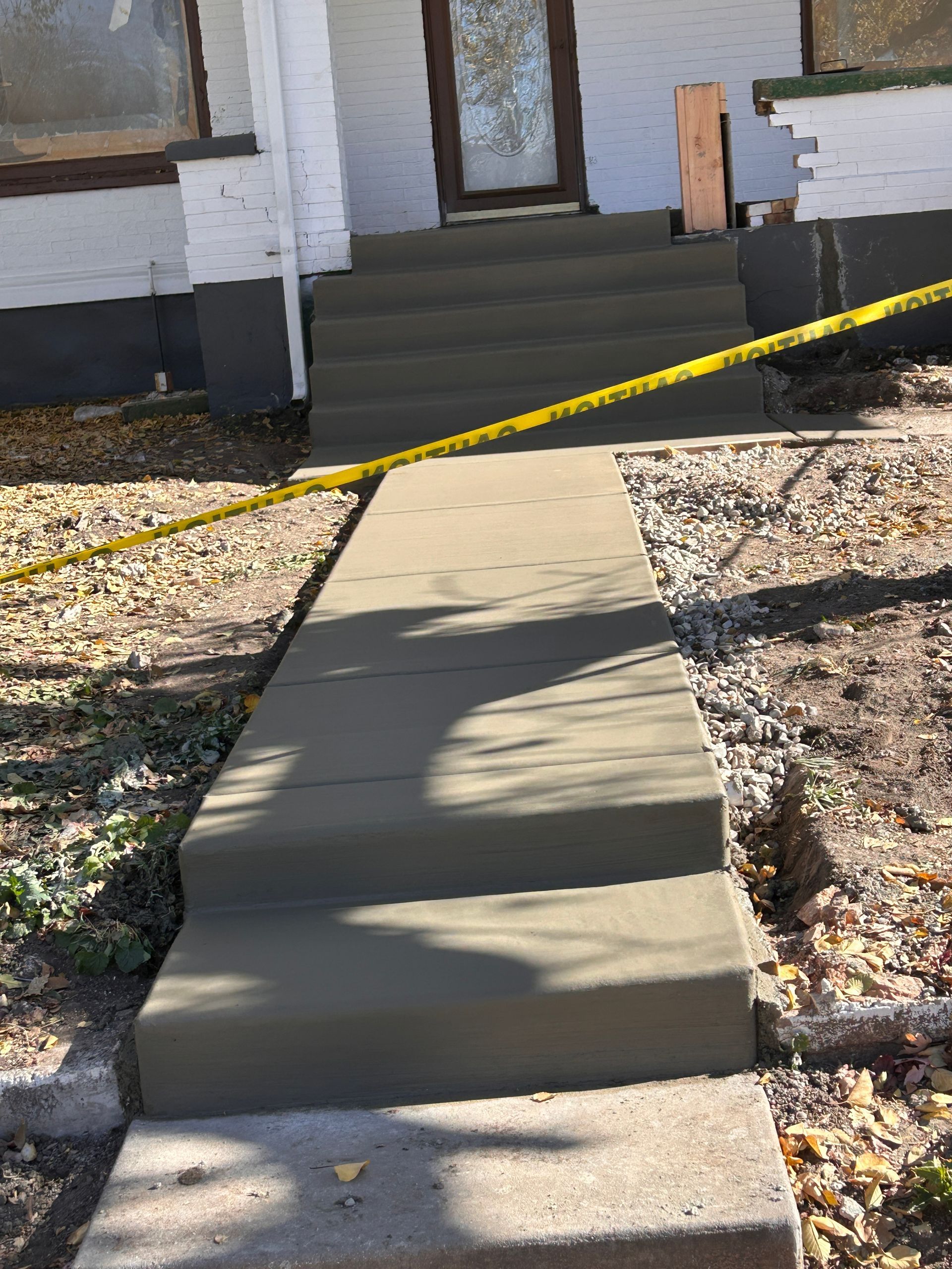 A newly poured concrete walkway leads to three freshly finished concrete steps at the front entrance of a white house.