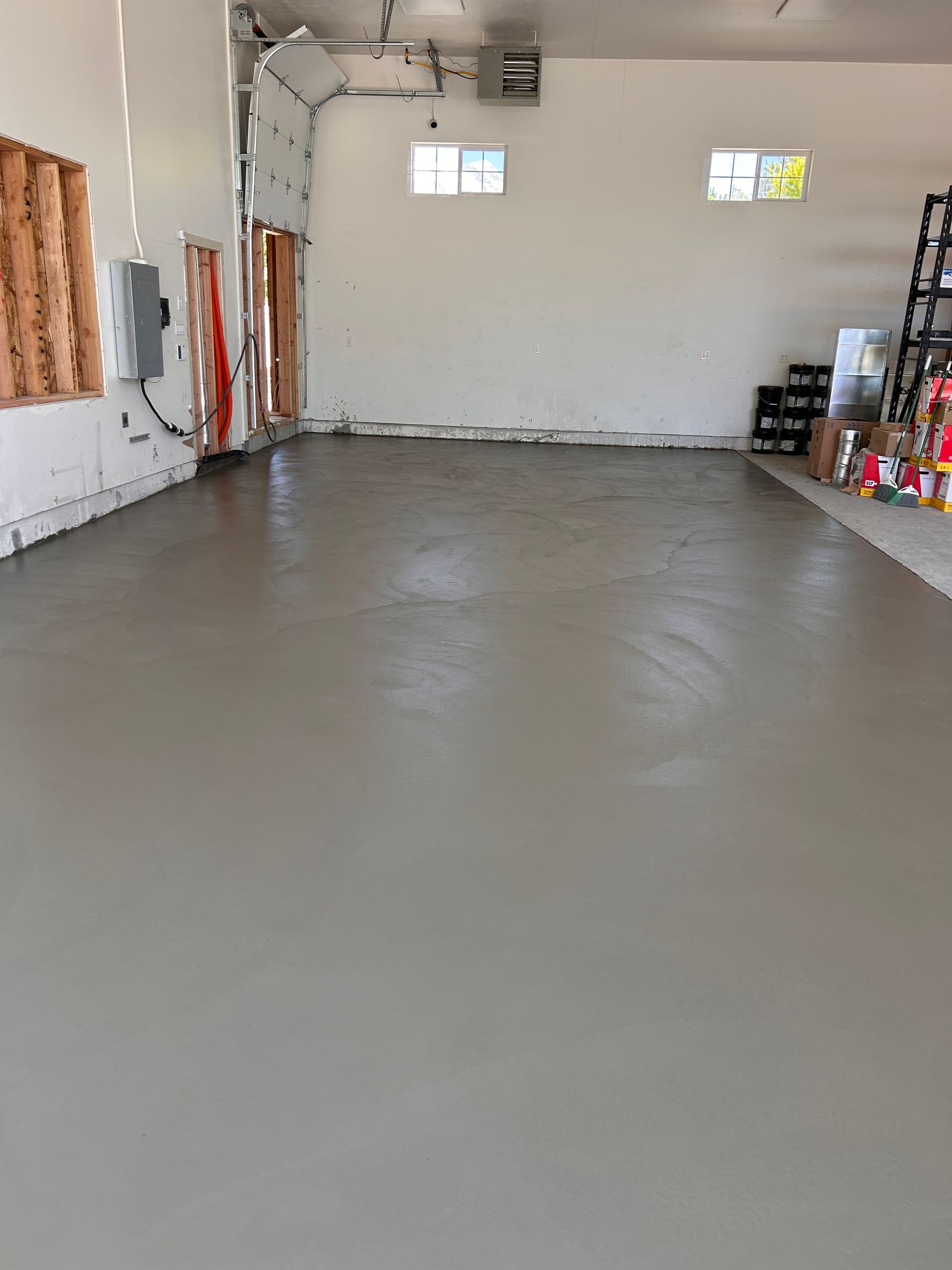 A wide shot of a garage with a freshly poured, smooth gray concrete floor, white walls, and open door mechanics.