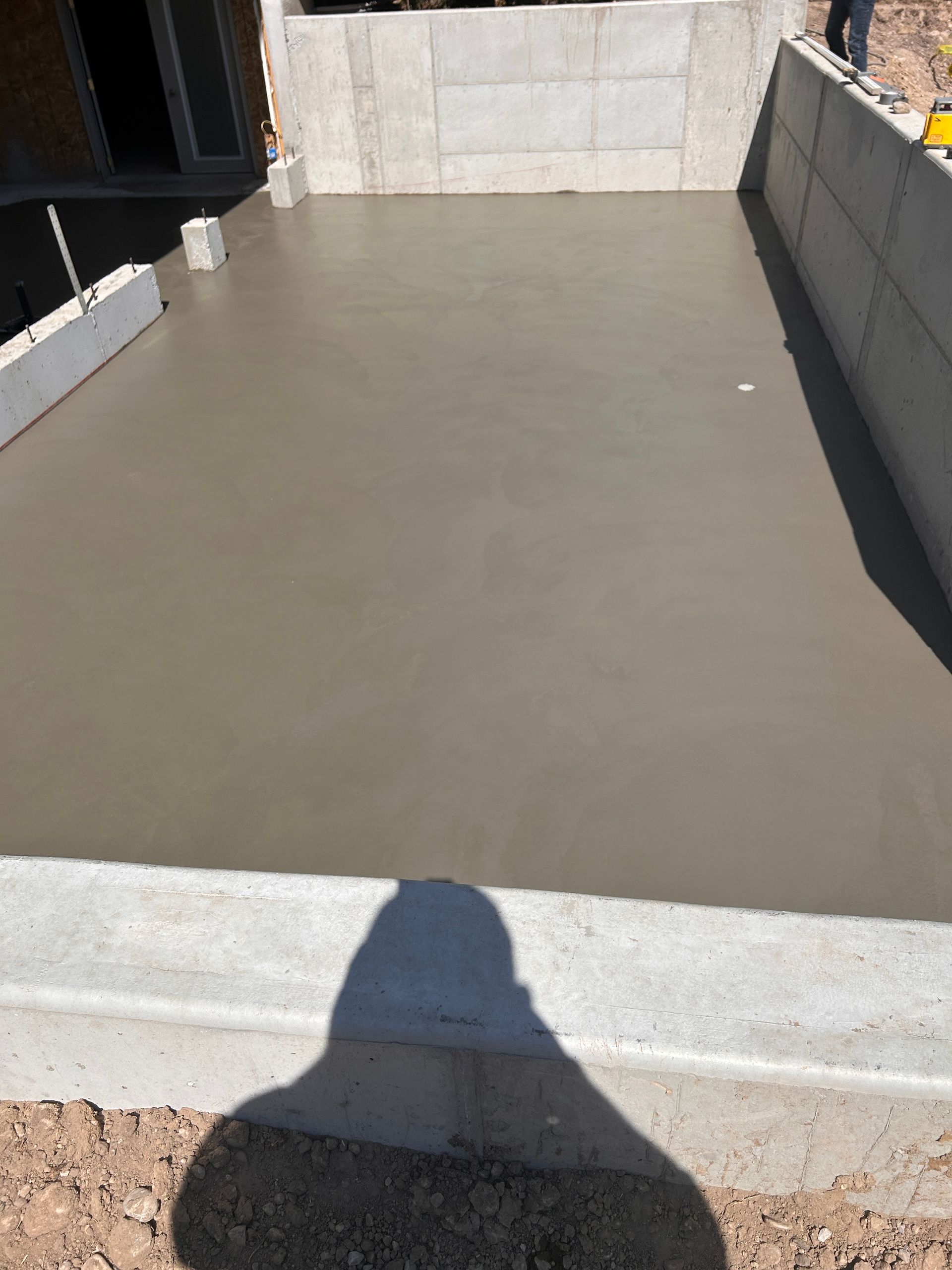 Freshly poured concrete slab surrounded by concrete block walls at a construction site.