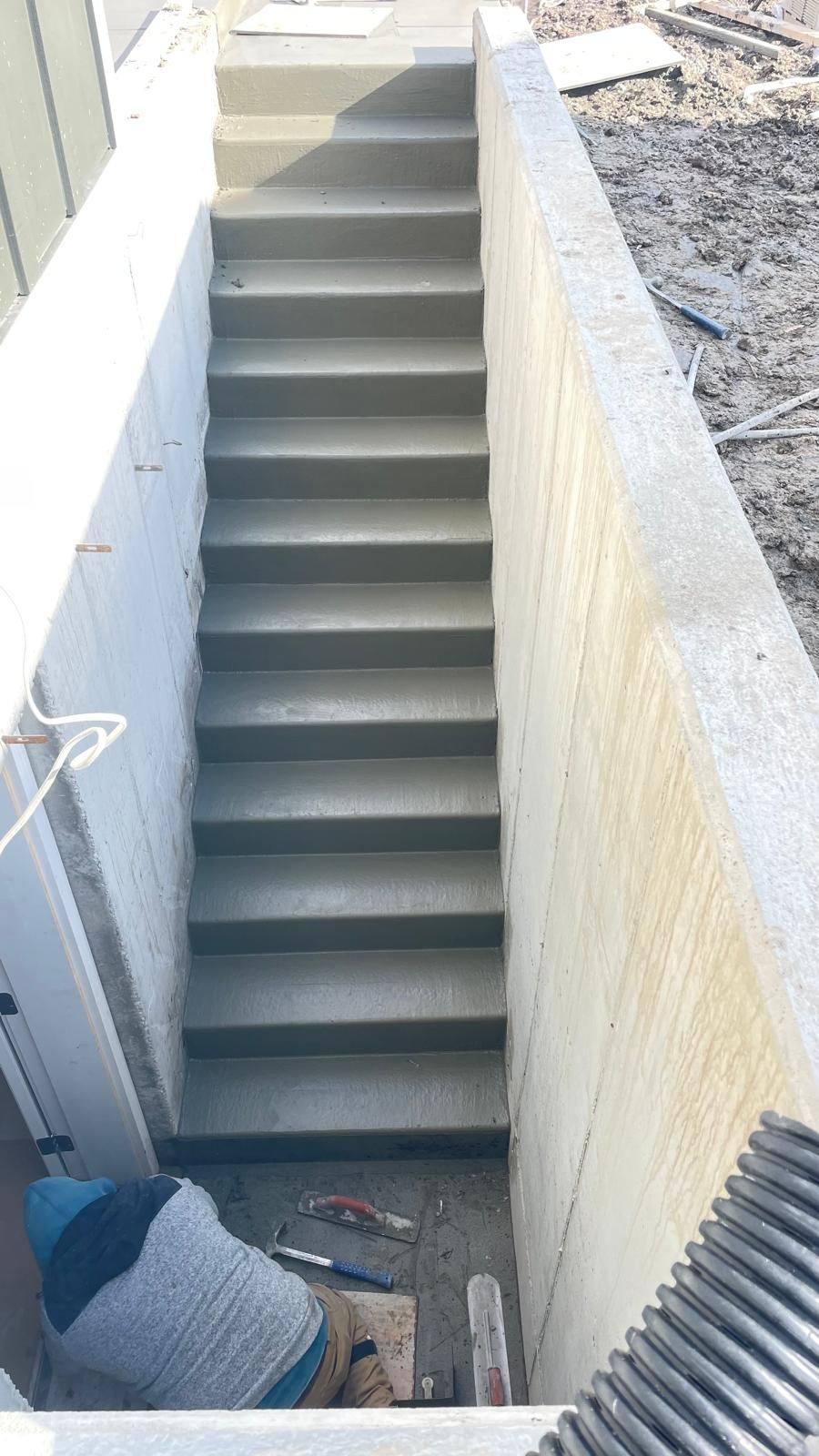A high-angle view of a newly poured concrete stairwell leading up to a landing, with a person working at the base.