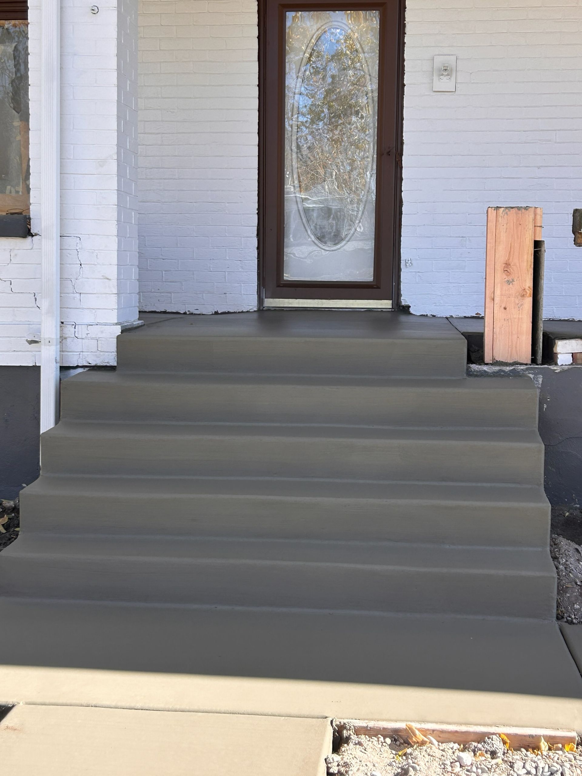 A set of newly poured, grey concrete steps leading up to a front door with a white brick exterior.