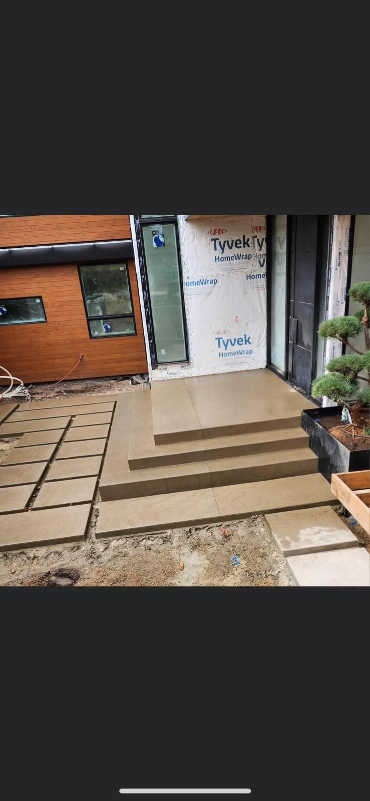 Modern concrete front steps with a landing leading to a house entrance, next to a paved walkway and wood siding.
