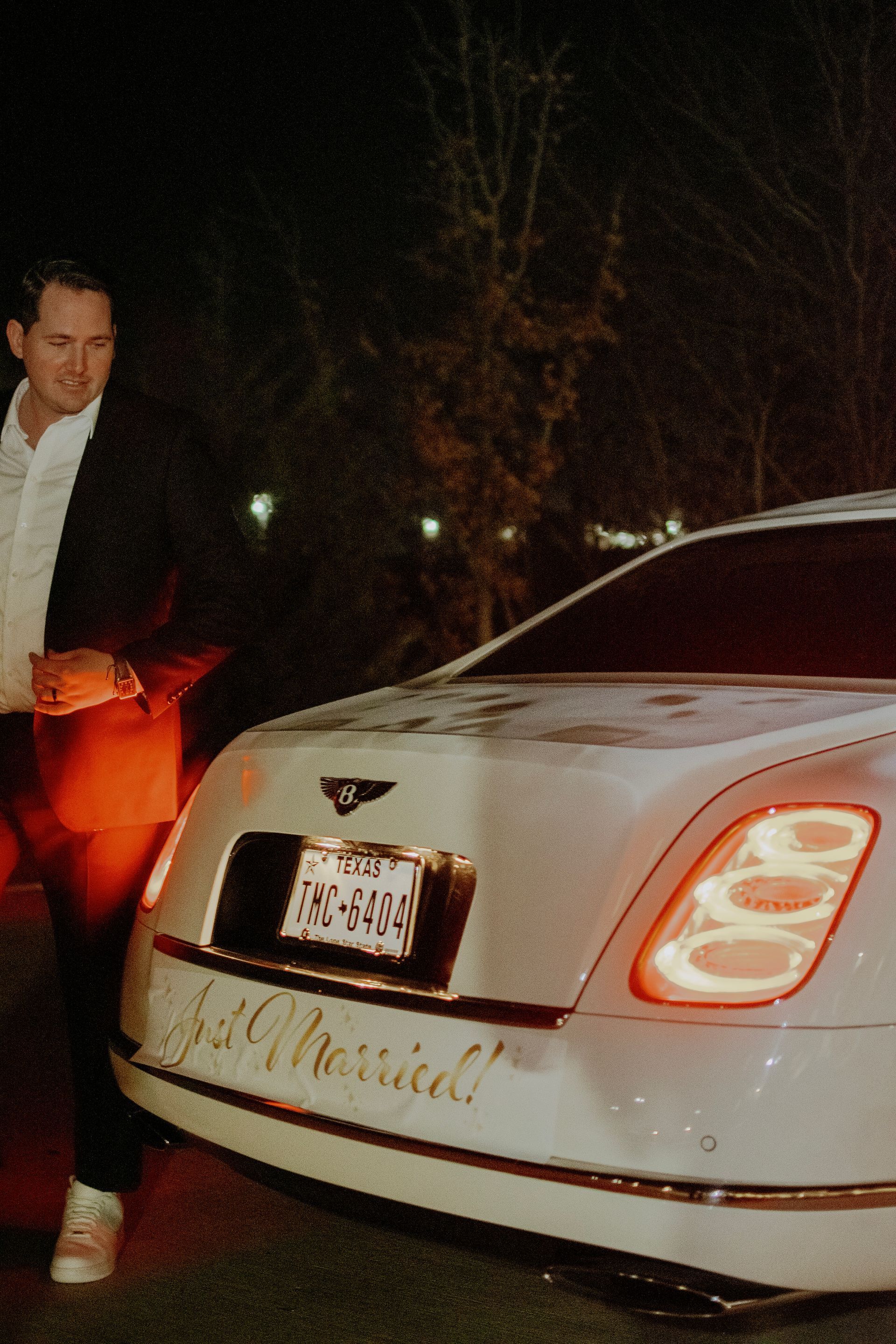 A man is standing next to a white car that says just married on the back
