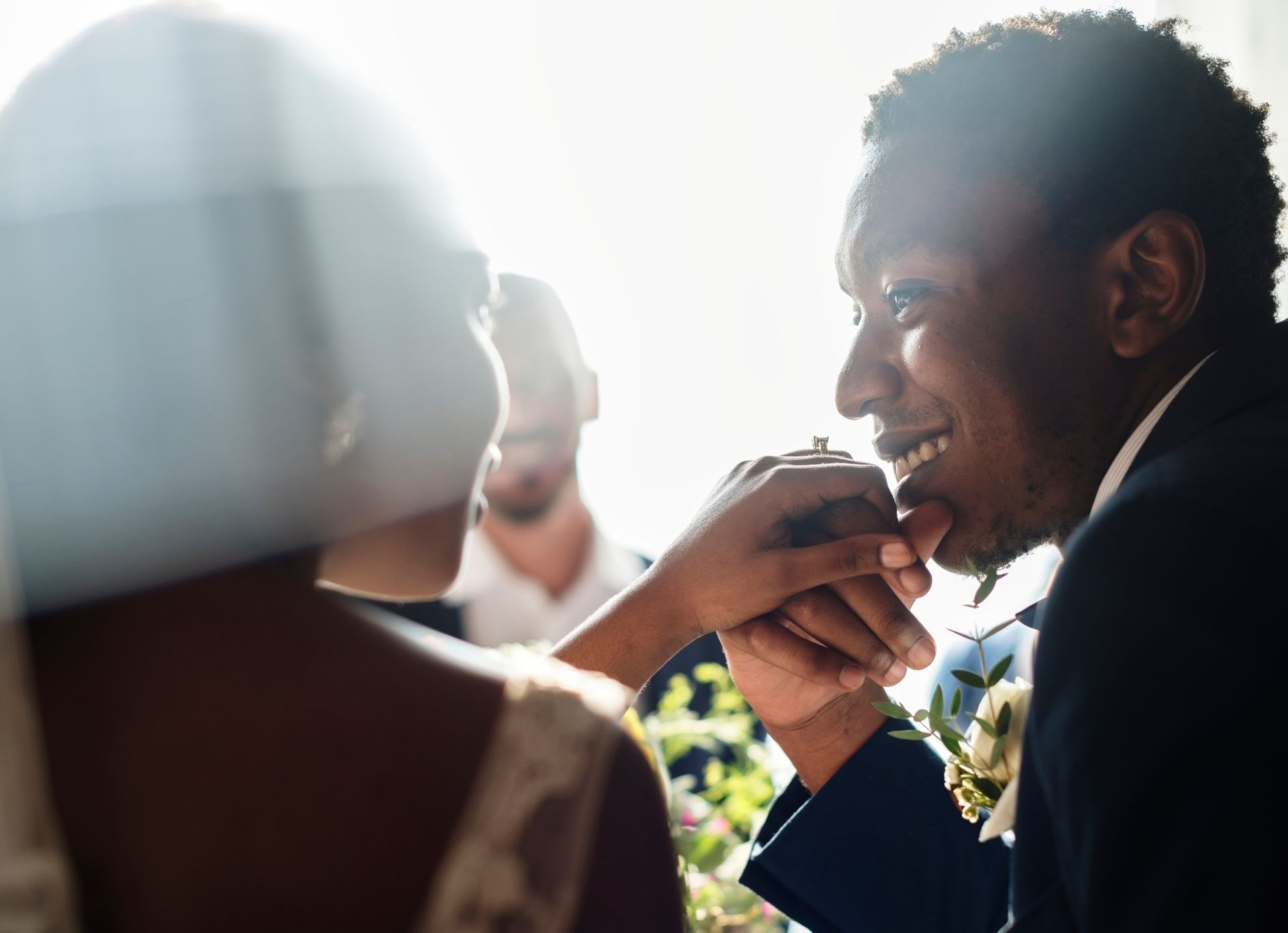 A person gently kissing their partner's hand at a wedding, with a bright, soft-focus, romantic atmosphere.