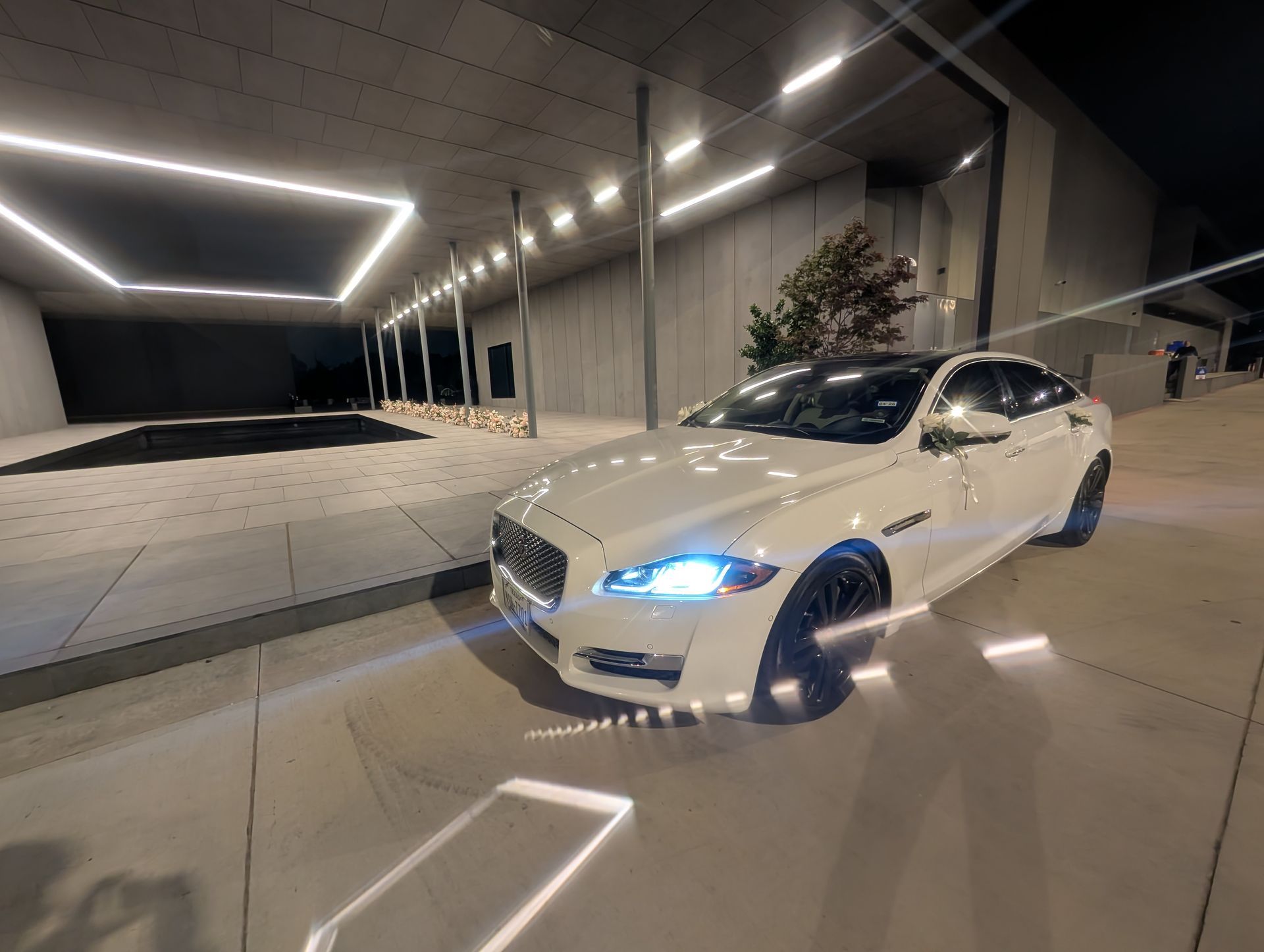 White sedan with blue headlights parked under modern geometric ceiling lights at night.