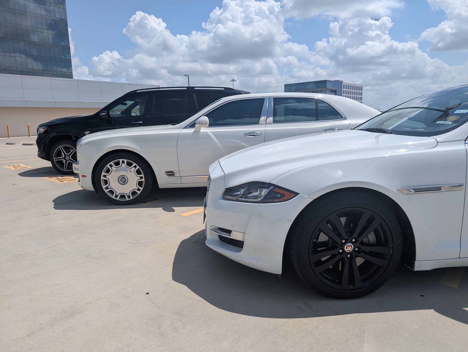 Three parked cars, including a white sedan in the foreground, on a sunny lot under a cloudy sky