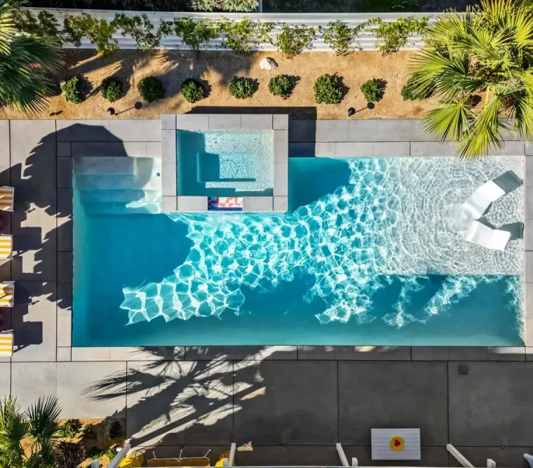 Aerial view of a backyard pool with lounge chairs, umbrellas, and tropical landscaping.