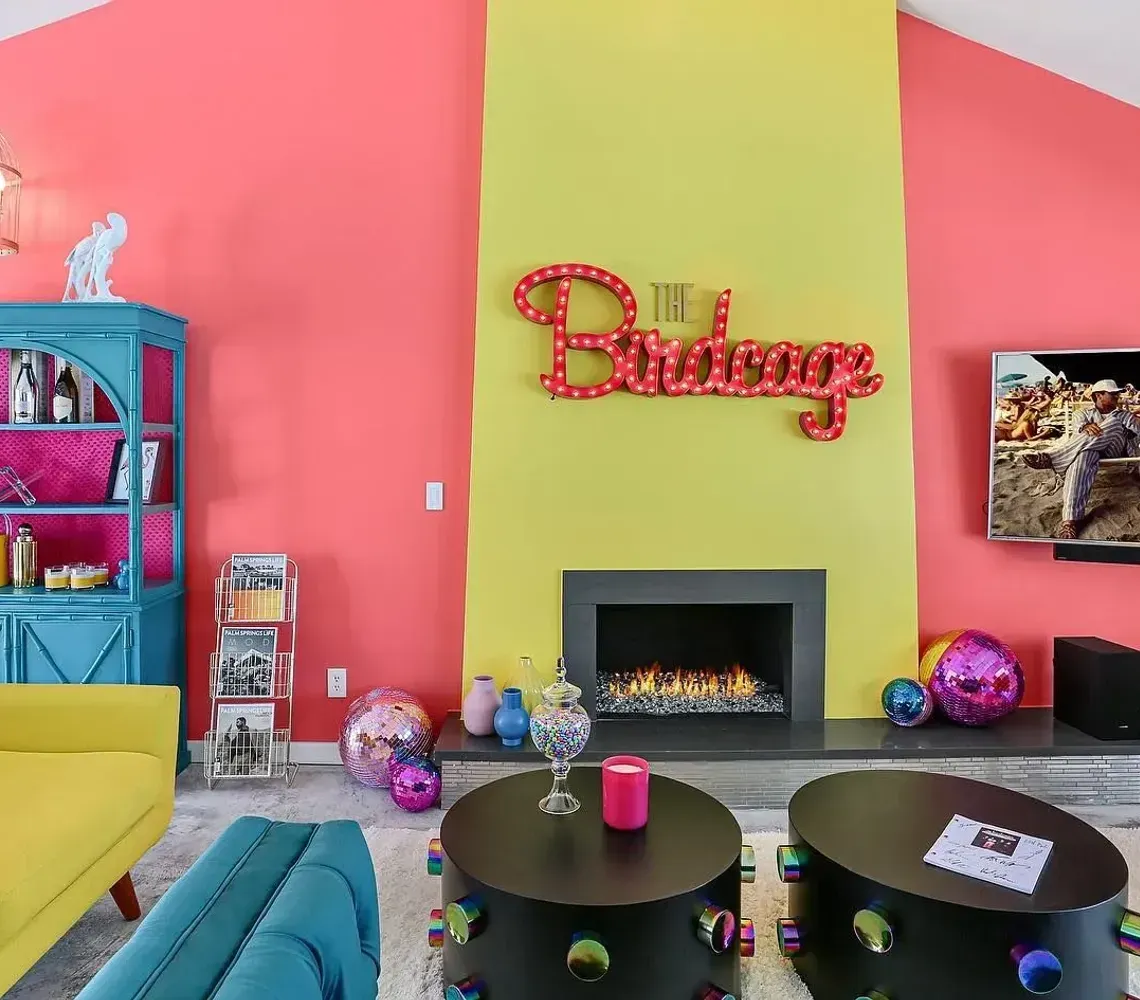 Bright living room with pink walls, yellow sofas, a teal shelf, and a fireplace under “The Bittangs” sign.