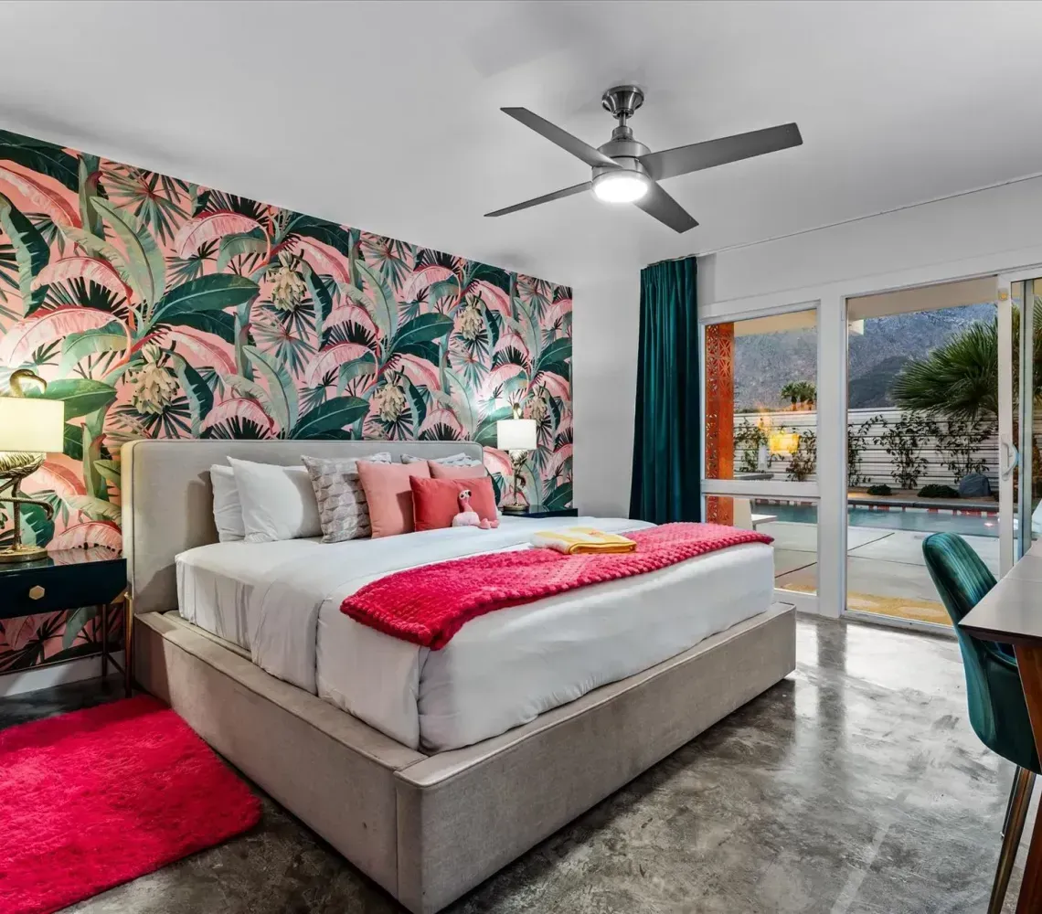 Bright bedroom with tropical wallpaper, pink accents, and sliding glass doors to a pool patio.