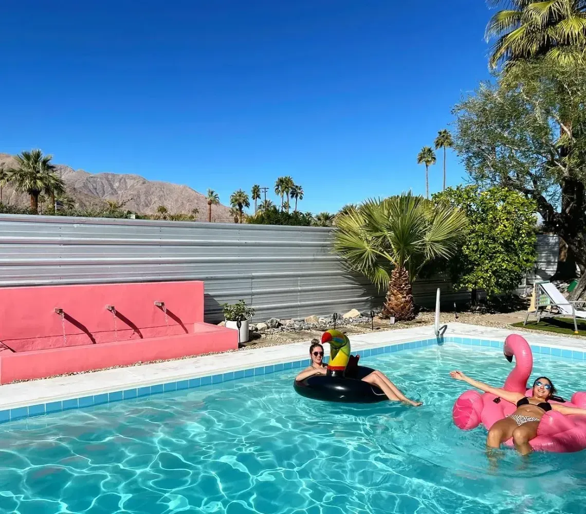 Backyard pool with two flamingo floaties, a swimmer on a black tube, and mountains in the background