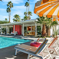 Mid-century poolside patio with striped lounge chairs, orange umbrella, and palm trees by a modern house
