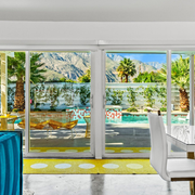 Bright living room with sliding glass doors opening to a sunny pool and palm-lined mountain view