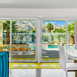 Bright living room with sliding glass doors opening to a sunny pool and palm-lined mountain view