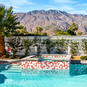 Turquoise pool with a patterned hot tub in front of a white fence and desert mountains