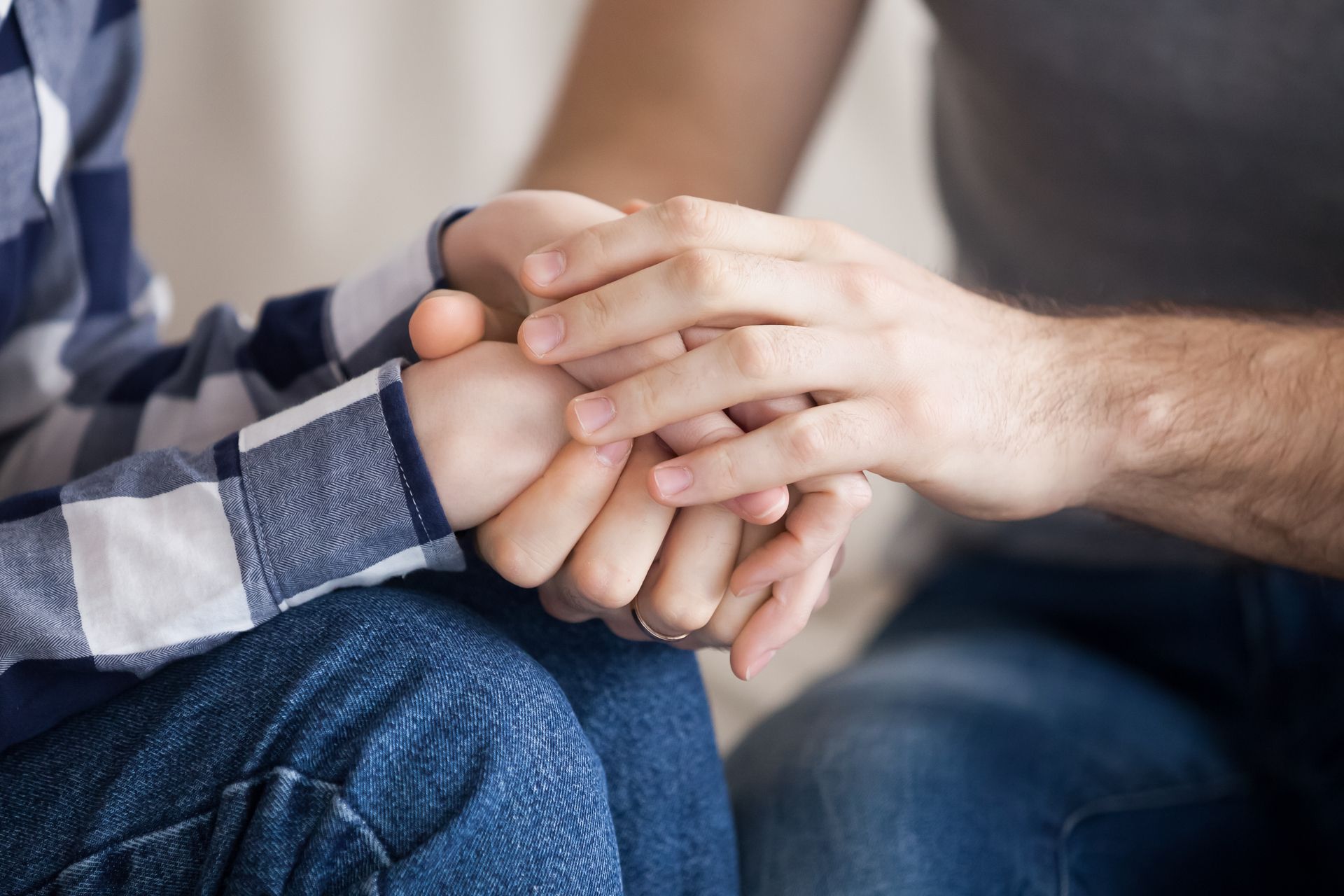 Hands gently holding a child’s hand on a couch, showing comfort and support