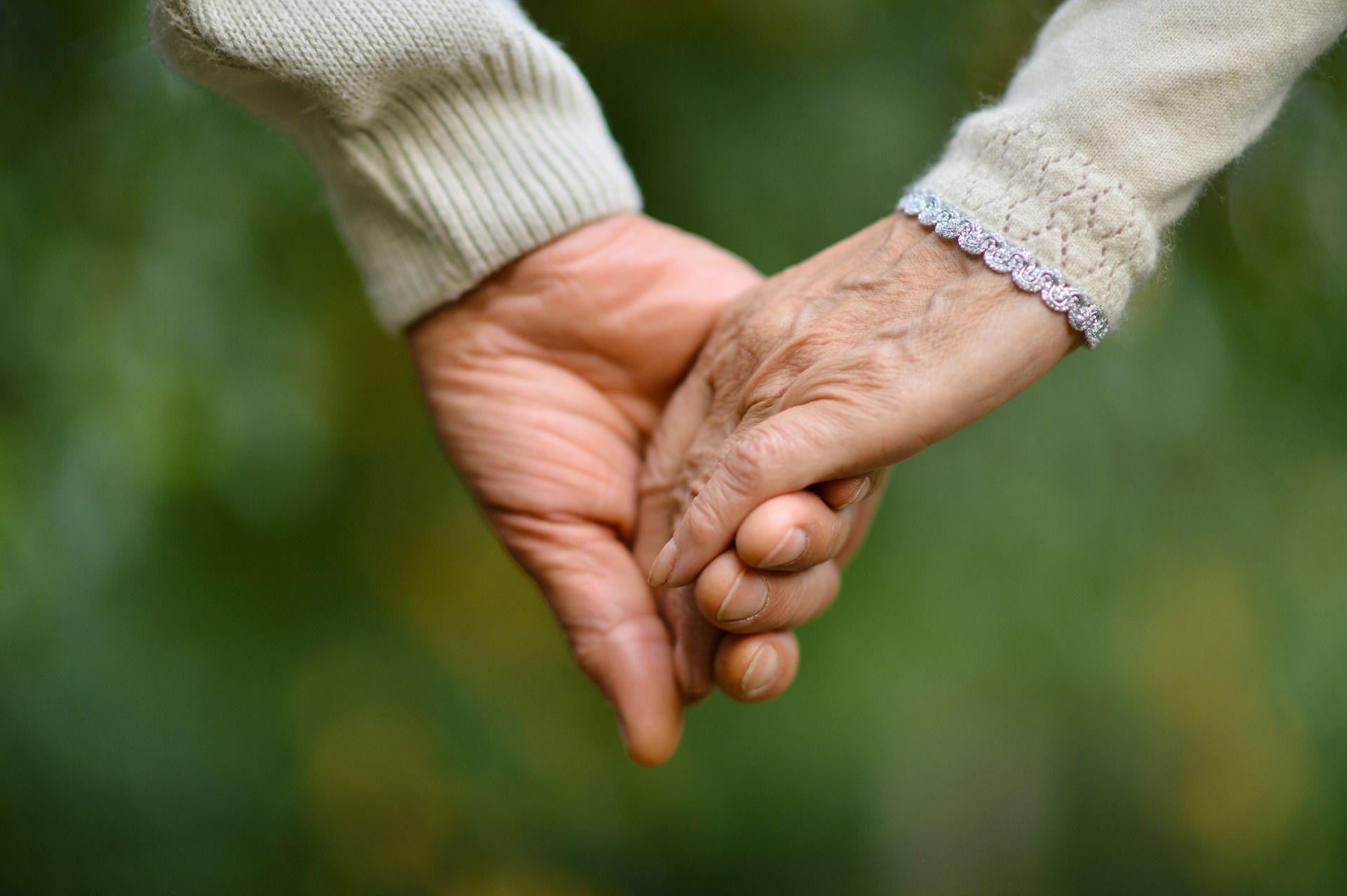 Two hands gently holding, one older and one younger, against a blurred green background