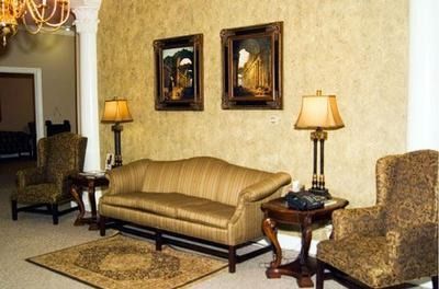 Elegant living room with gold sofa, armchairs, lamps, and framed wall art on patterned rug.
