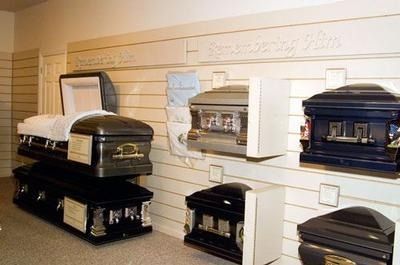Display of assorted black and white caskets on shelves in a funeral home showroom