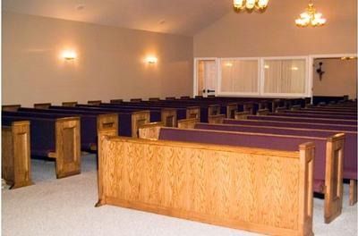 Empty church sanctuary with wooden pews, purple cushions, and soft wall lighting