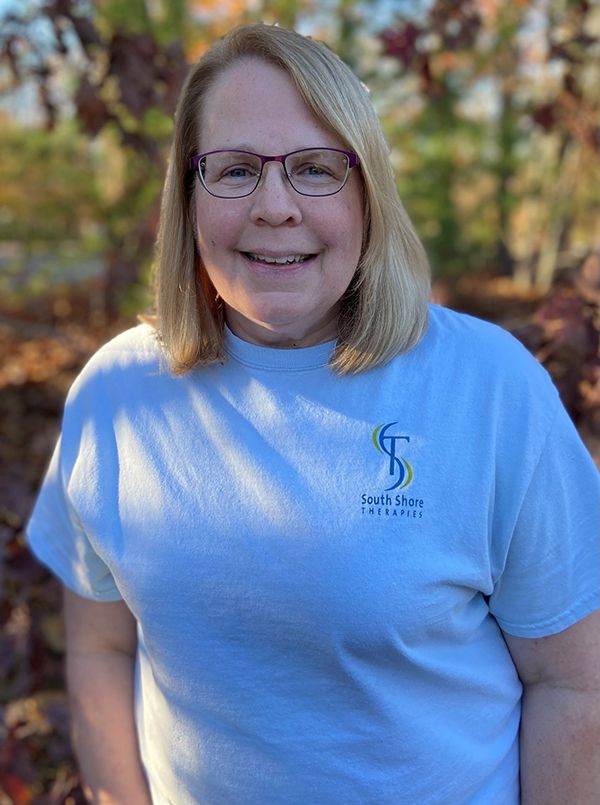 Smiling person in glasses and a light blue T-shirt standing outdoors in sunlight