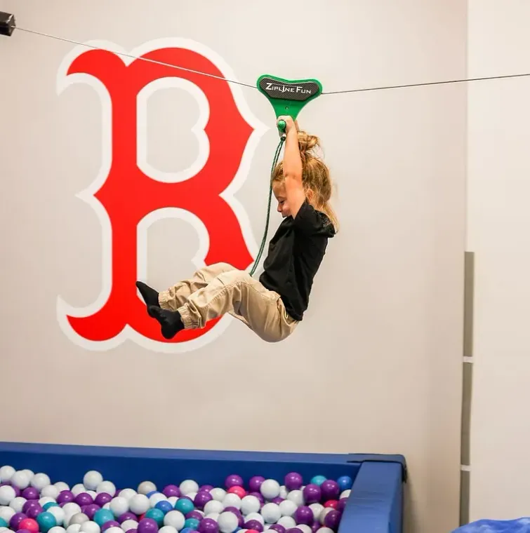 Child swinging from a zip line beside a large red “B” in a play area