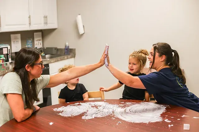 Four people around a table high-five over a flour-covered mess in a kitchen