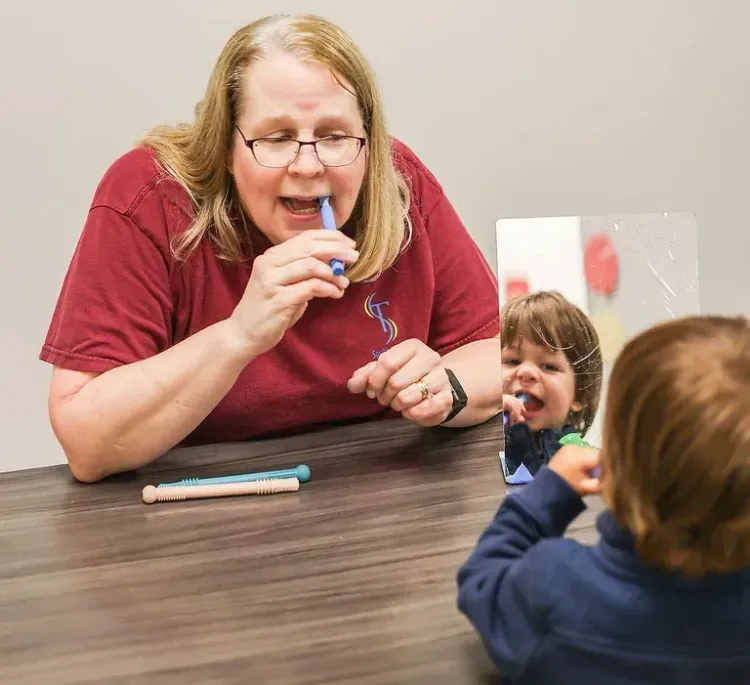 Woman demonstrating a toothbrush to a child during a dental lesson at a table