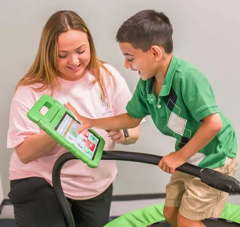 Teacher and child using a green tablet together, smiling in a classroom-like setting