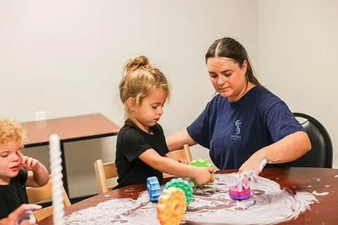 Children playing with colorful sensory toys at a table with an adult guiding them