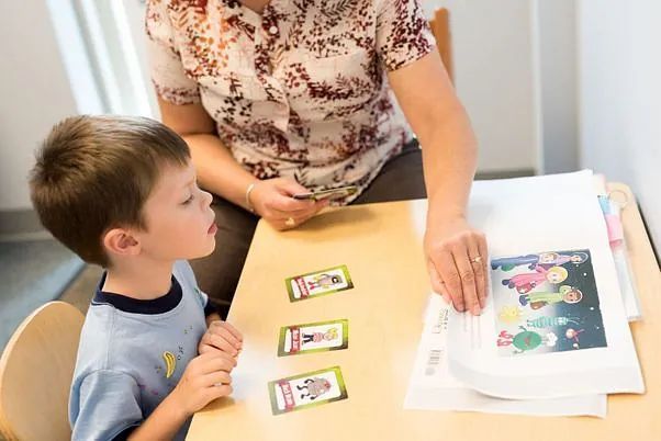 Adult and child at a table, looking at picture cards beside a colorful worksheet
