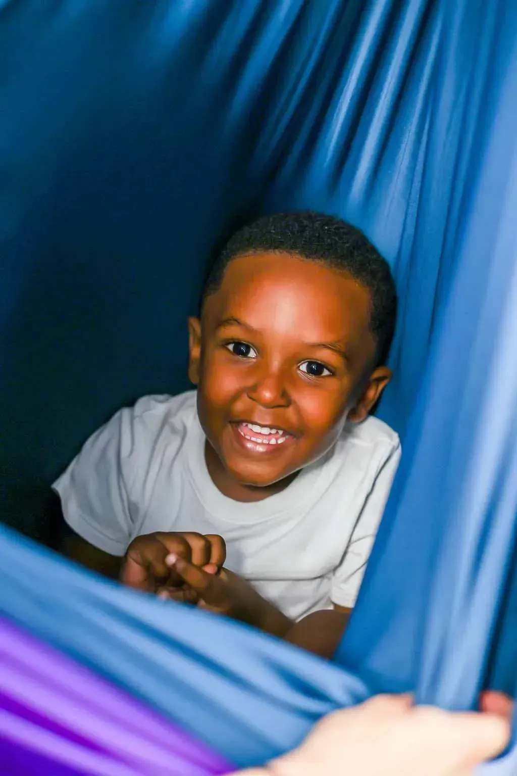 Smiling child peeking out from blue fabric drapes